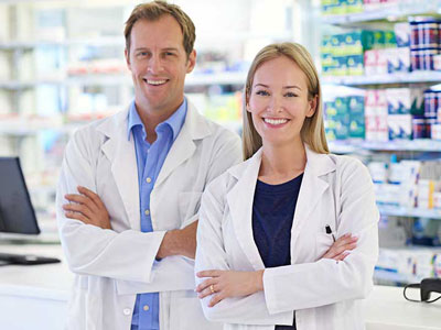 Male and Female pharmacists in lab coats standing next to each other and smiling 